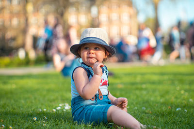 Cute baby boy looking away while sitting on field