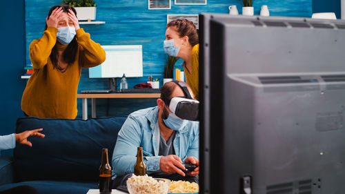 Man playing video game while wearing virtual reality simulator by women at home