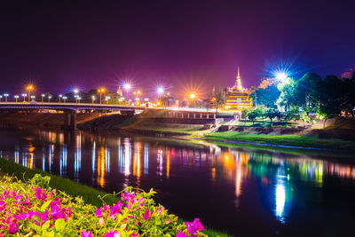 Illuminated bridge by river against sky at night