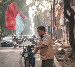 Side view of young man holding umbrella standing on street in city