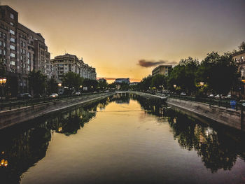 Bridge over river amidst buildings in city at sunset