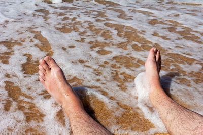 Men's legs on a sandy beach in the sea waves