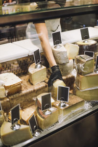 Midsection of female retail clerk removing cheese from display cabinet at grocery store