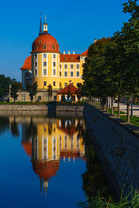 Reflection of building in lake against clear blue sky