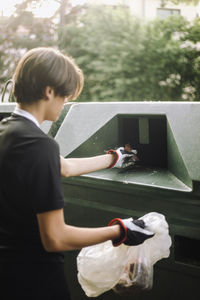 Teenage boy putting plastic garbage in recycling bin