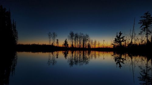 Reflection of silhouette trees in lake against blue sky