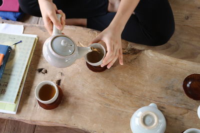 High angle view of person pouring green tea in cup at home