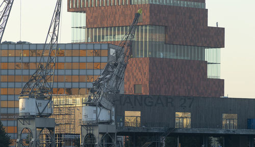 Low angle view of crane by building against sky