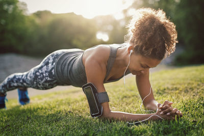 Woman doing plank exercise on grassy field at park