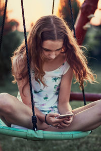 Girl using mobile phone while sitting on swing