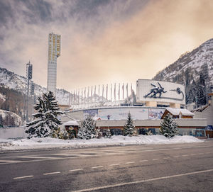 Snow covered road by buildings against sky