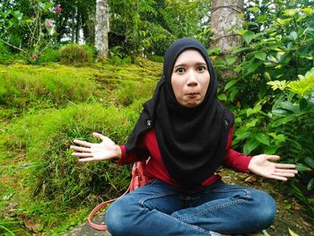 Portrait of young woman sitting against trees