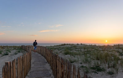 Rear view of man looking at sea on footpath against sky during sunset