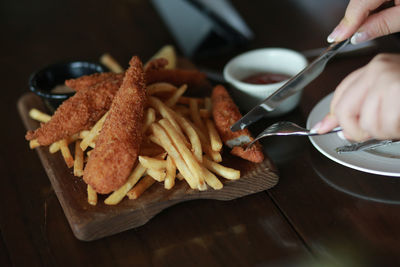 Cropped hands of woman eating fish and chips at wooden table