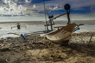 Outrigger boat moored on shore at beach against sky