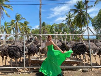 Woman standing by palm trees and plants against sky