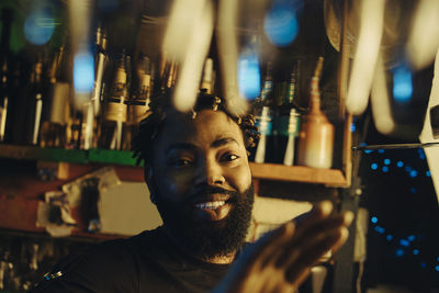 Portrait of smiling bartender with afro hairstyle at illuminated