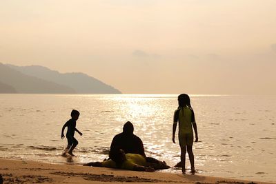 People at beach against sky during sunset