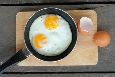 Directly above shot of fried egg in frying pan on cutting board over table