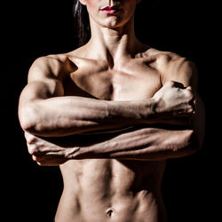 Midsection of shirtless man standing against black background