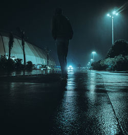 Rear view of man standing on wet street at night