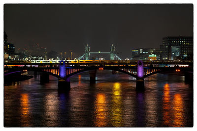 Illuminated bridge over river in city at night