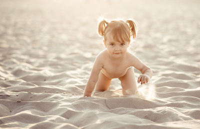 Portrait of cute girl crawling on sand at beach