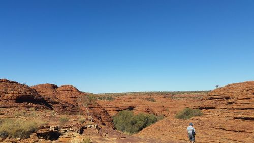 Rear view of woman standing on rock formations against clear blue sky