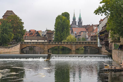 Bridge over river by buildings in city against sky