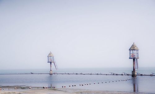 Lighthouse by sea against clear sky