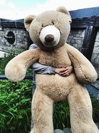 Cropped hands of person holding large teddy bear against wall