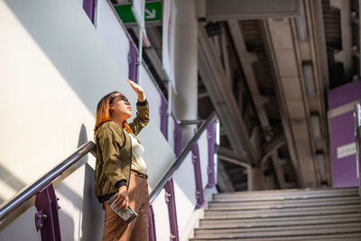 Low angle view of woman shielding eyes while standing on staircase