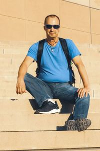 Portrait of young man wearing sunglasses sitting against wall