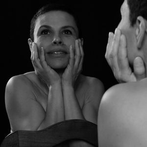 Reflection of topless woman holding her face while looking away