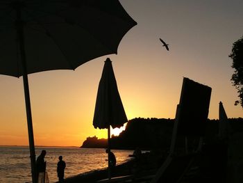 Silhouette people at beach against sky during sunset