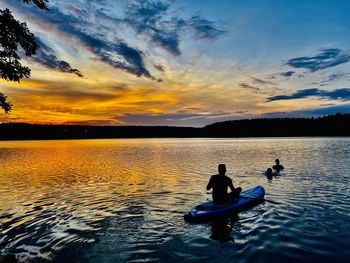 Silhouette people in lake against sky during sunset