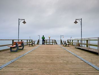 Rear view of man on pier by sea against sky