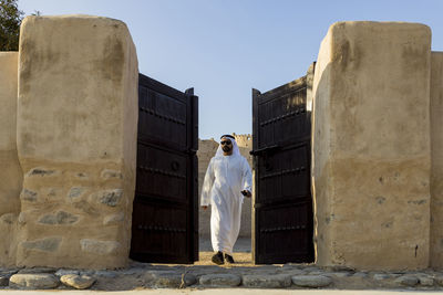 Full length of man in traditional dress walking outside gate against sky