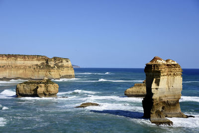 Rock formation in sea against clear blue sky