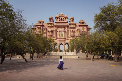 Back view of anonymous female traveler walking on pavement towards aged patrika gate building on sunny day in jaipur, india