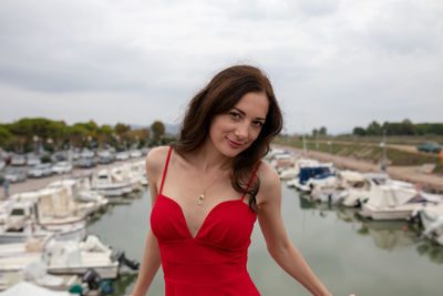 Portrait of woman in red dress standing against harbor in city