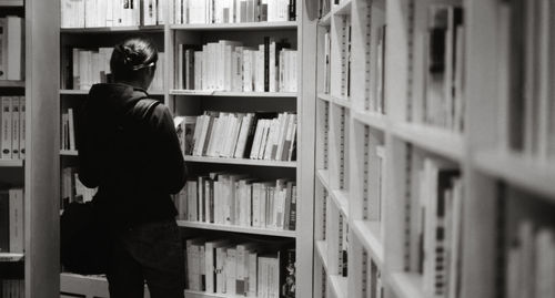 Rear view of woman standing by shelves in library