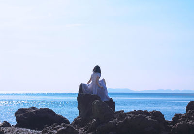 Man sitting on rock by sea against clear sky