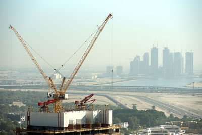 Cranes by buildings against sky in city