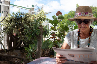 Senior woman reading newspaper against plants