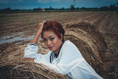 Portrait of woman sitting on hay bale at field