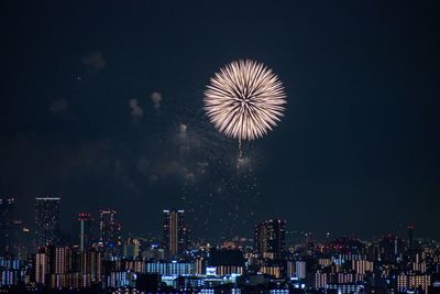 Firework display in city against sky at night