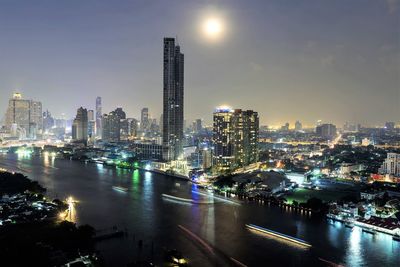 Illuminated buildings by river against sky in city at night