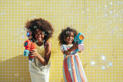 Happy sisters playing with bubble guns on sunny day