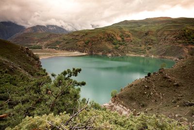 Scenic view of green lake and mountains against sky